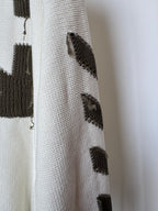 Off-white sweater sleeve with small black geometric knit patches