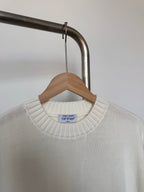 Off-white knit sweater with ribbed crew neck and small black brand label on collar