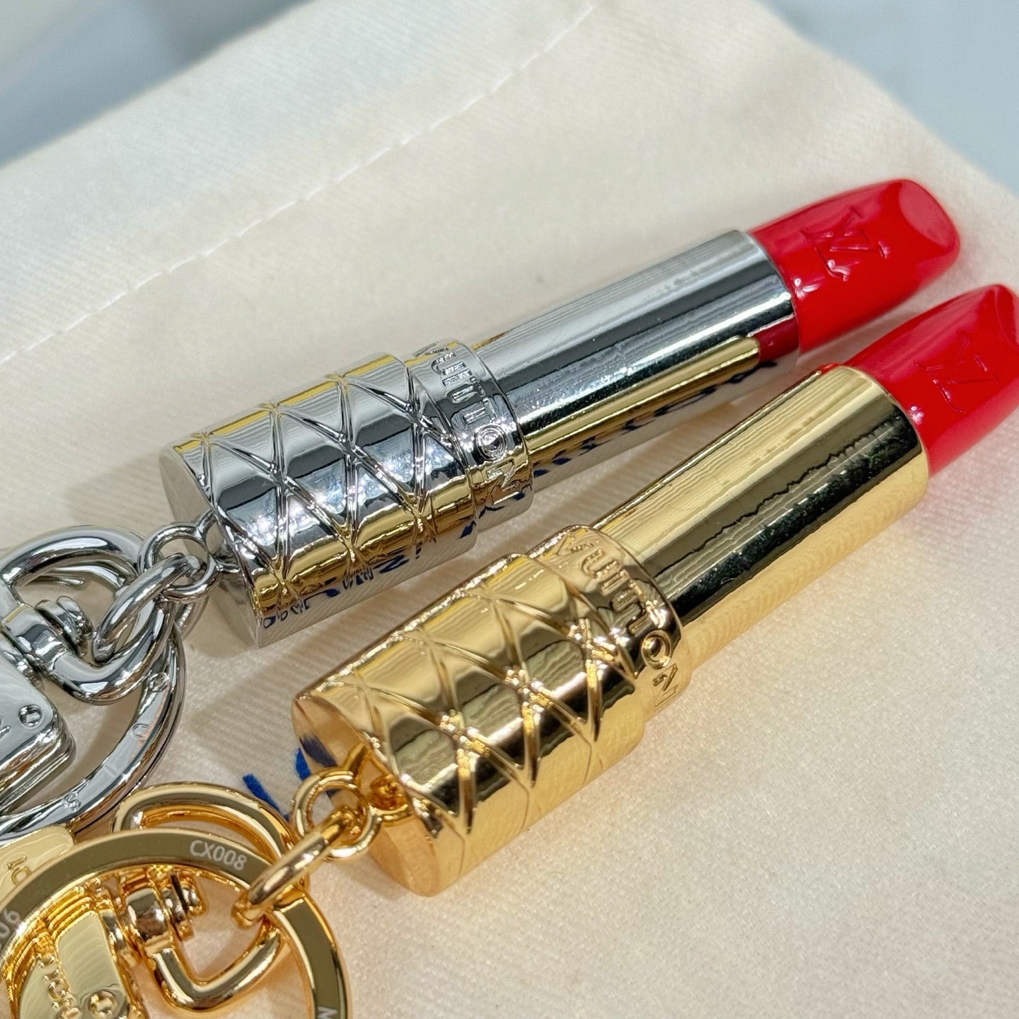Two lipstick-shaped keychains on pouch: silver and gold bodies with red caps