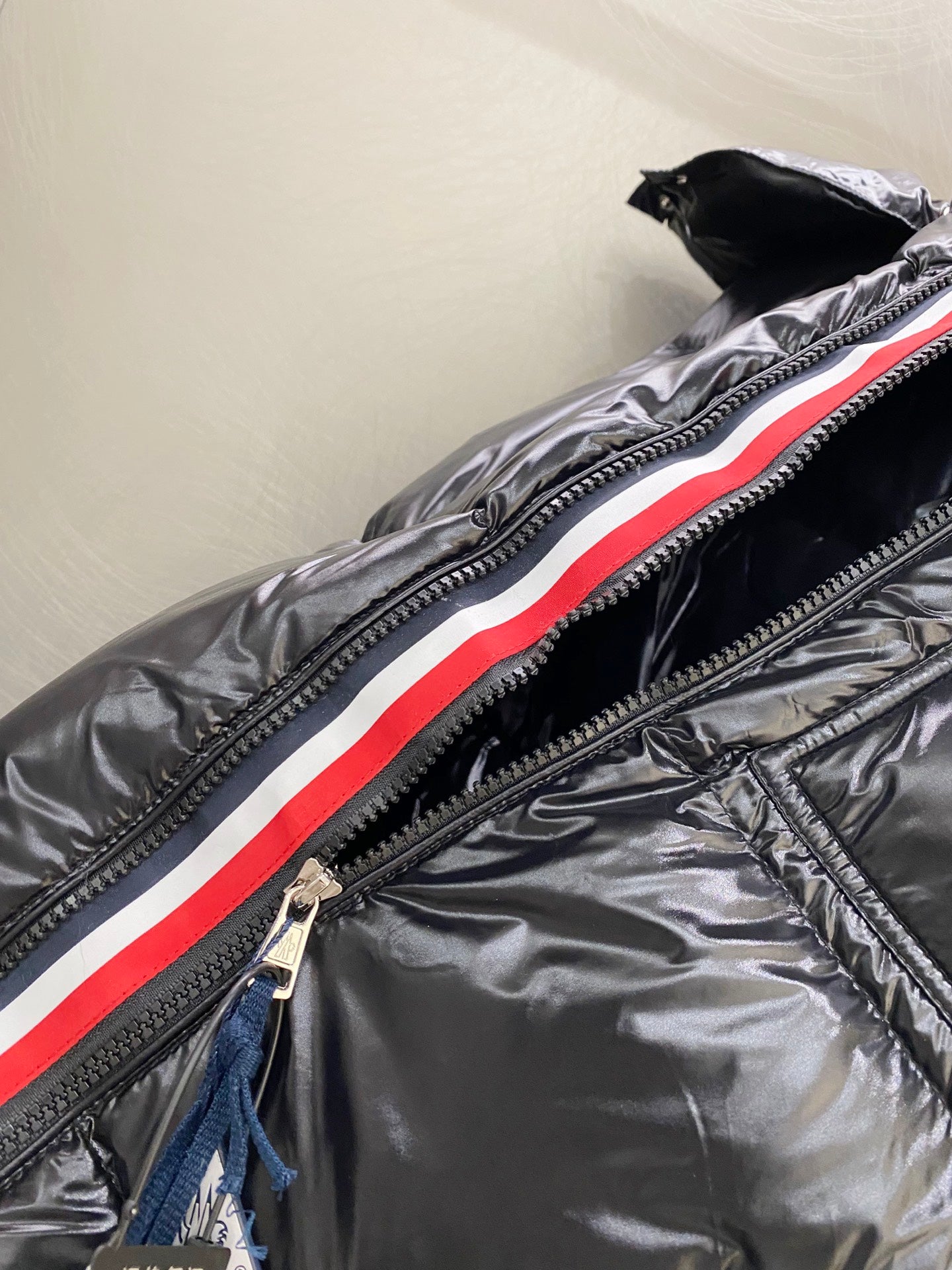 Moncler long padded jacket close-up: dark front zipper with red and white stripe