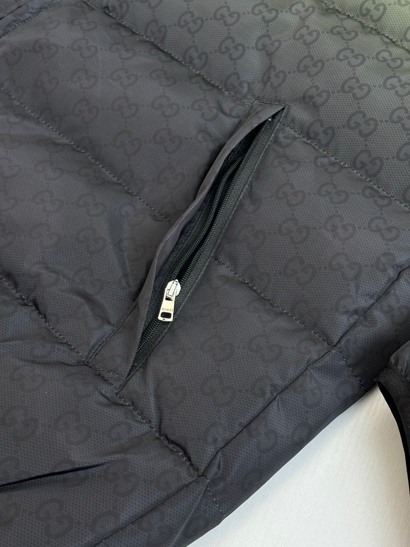 Dark monogram puffer jacket sleeve panel with zipper seam and pull tab