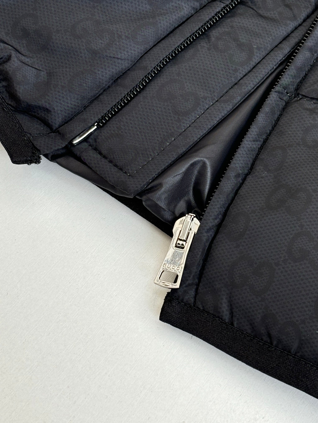 Dark puffer jacket zipper with metal pull and monogram texture