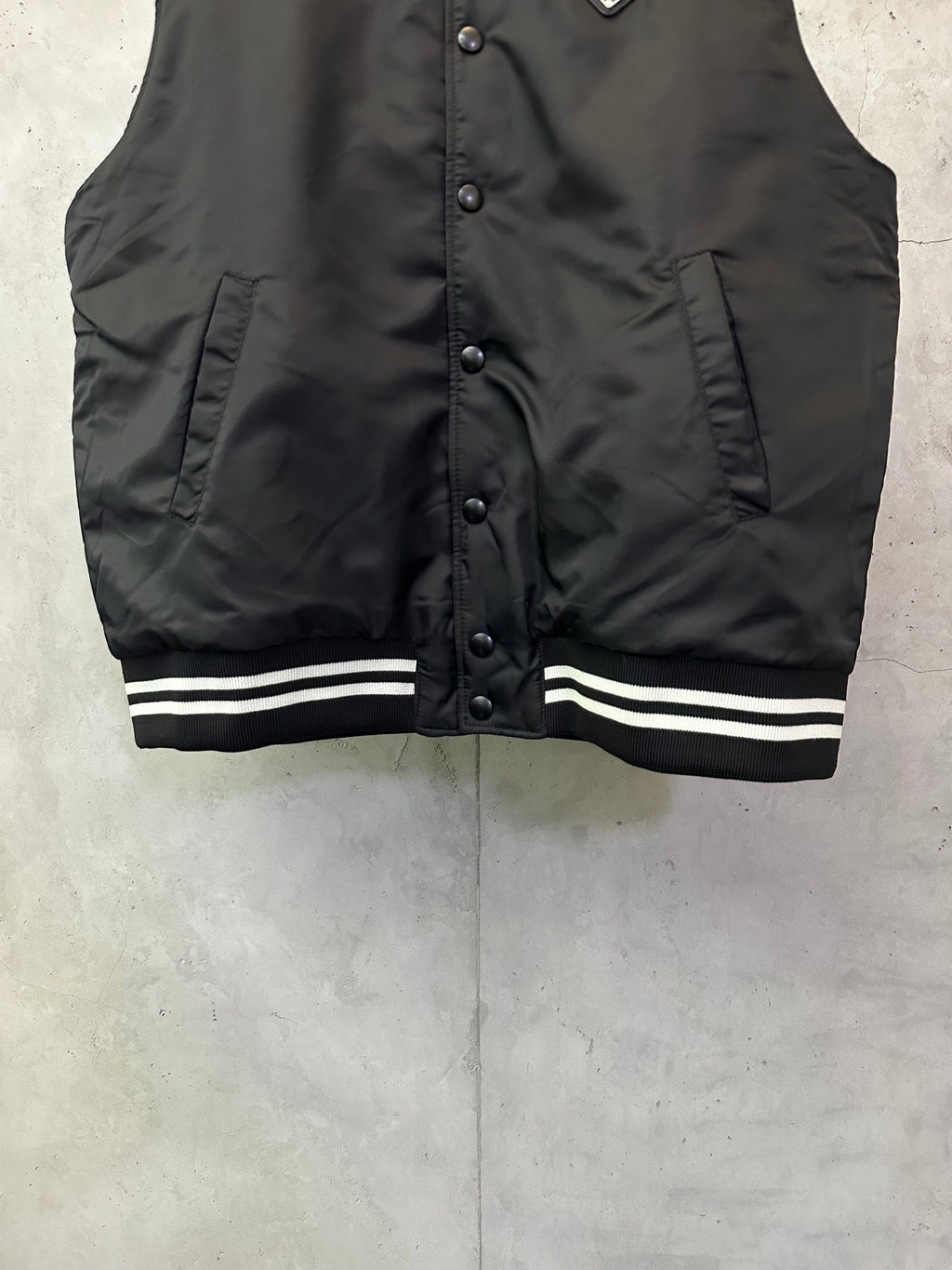 Sleeveless dark bomber vest with snap buttons and striped ribbed hem