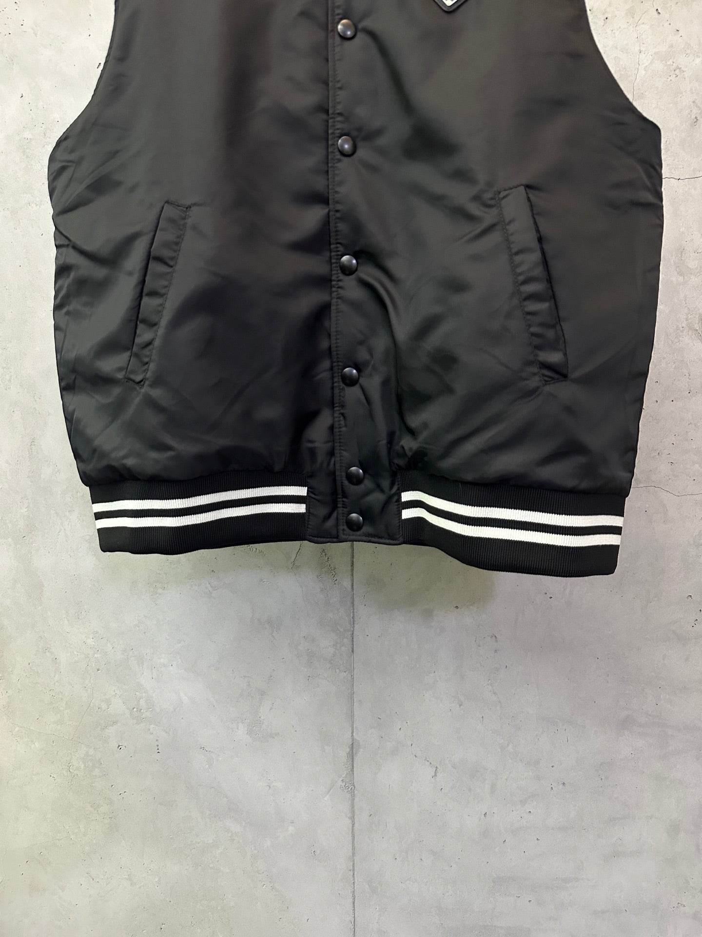 Sleeveless dark bomber vest with snap buttons and striped ribbed hem