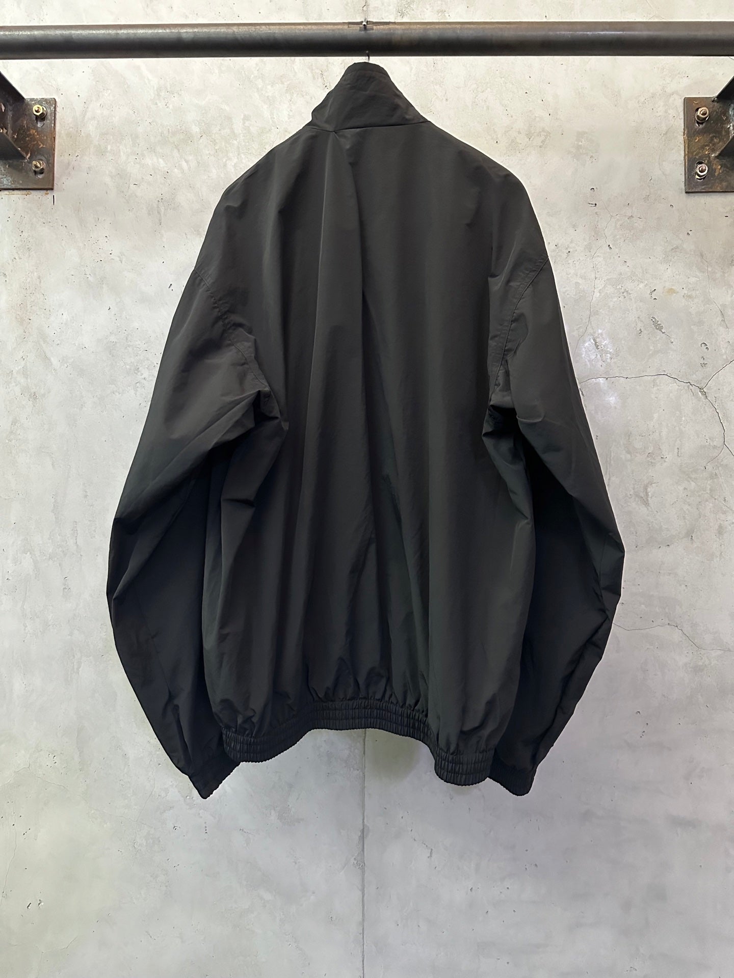 Black long bomber jacket, back view, relaxed shoulders, gathered hem cuffs