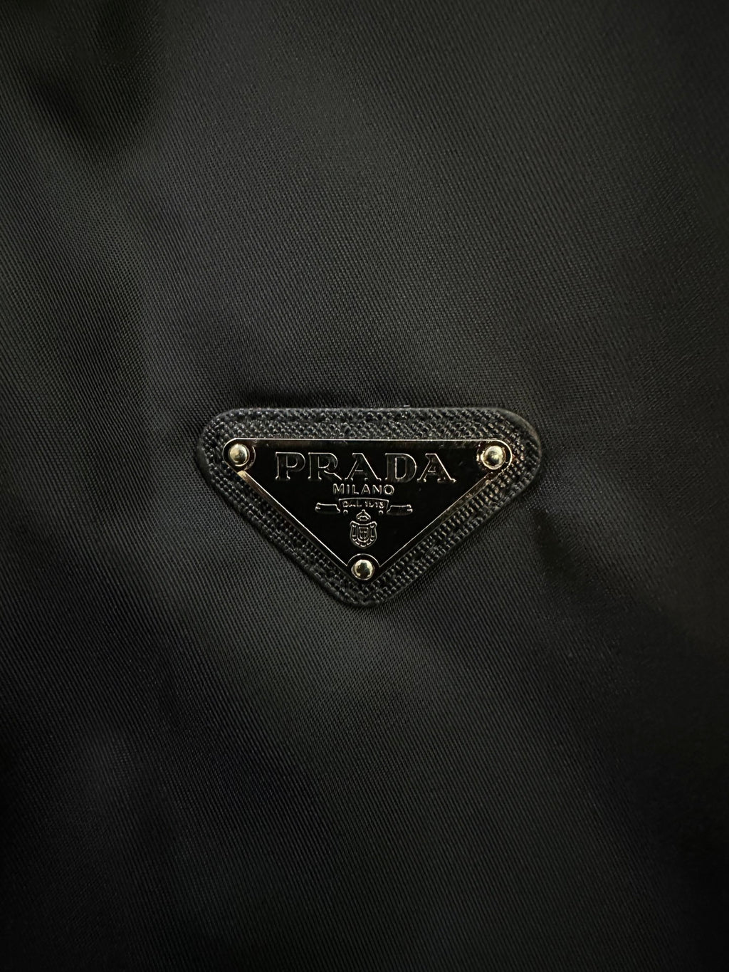 Prada triangular logo patch on dark fabric