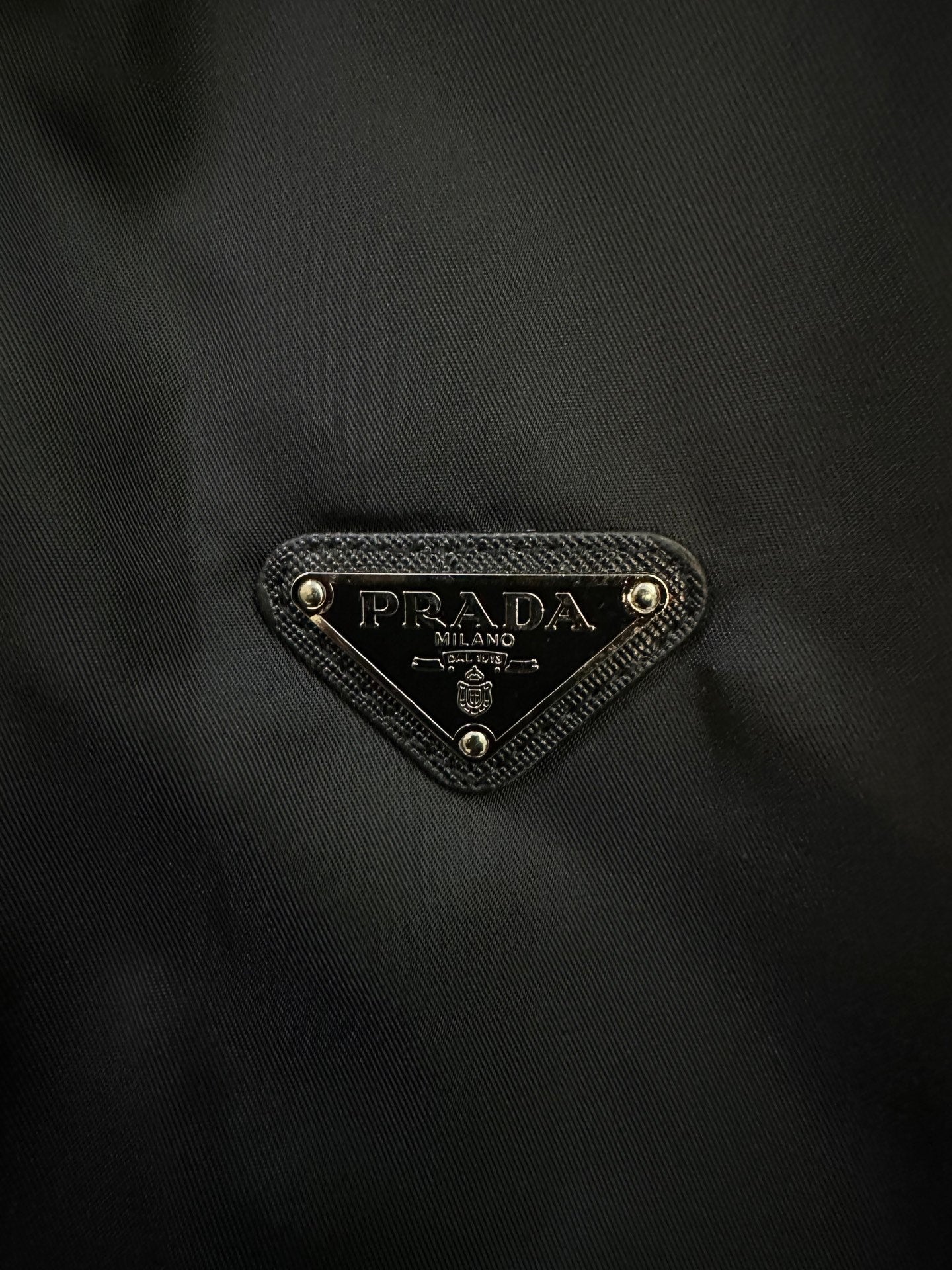 Prada triangular logo patch on dark fabric
