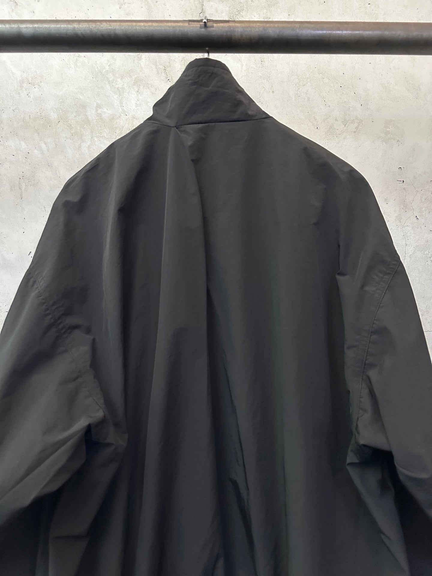 Black long bomber jacket, high collar/hood shape, pleated back
