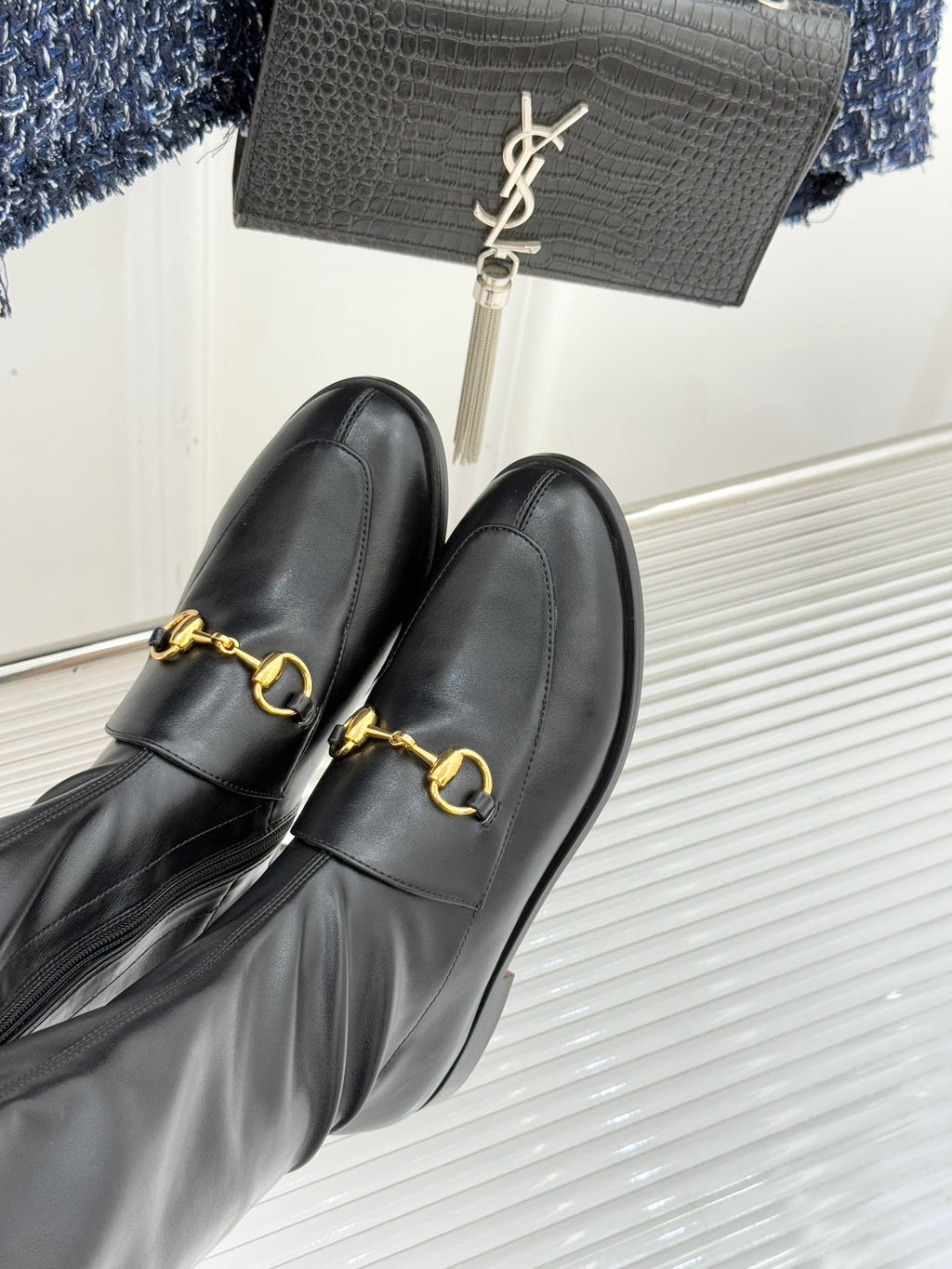 Black leather boots with gold horsebit buckle detail, close-up side view