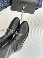 Black leather boots with gold horsebit buckle detail, close-up side view