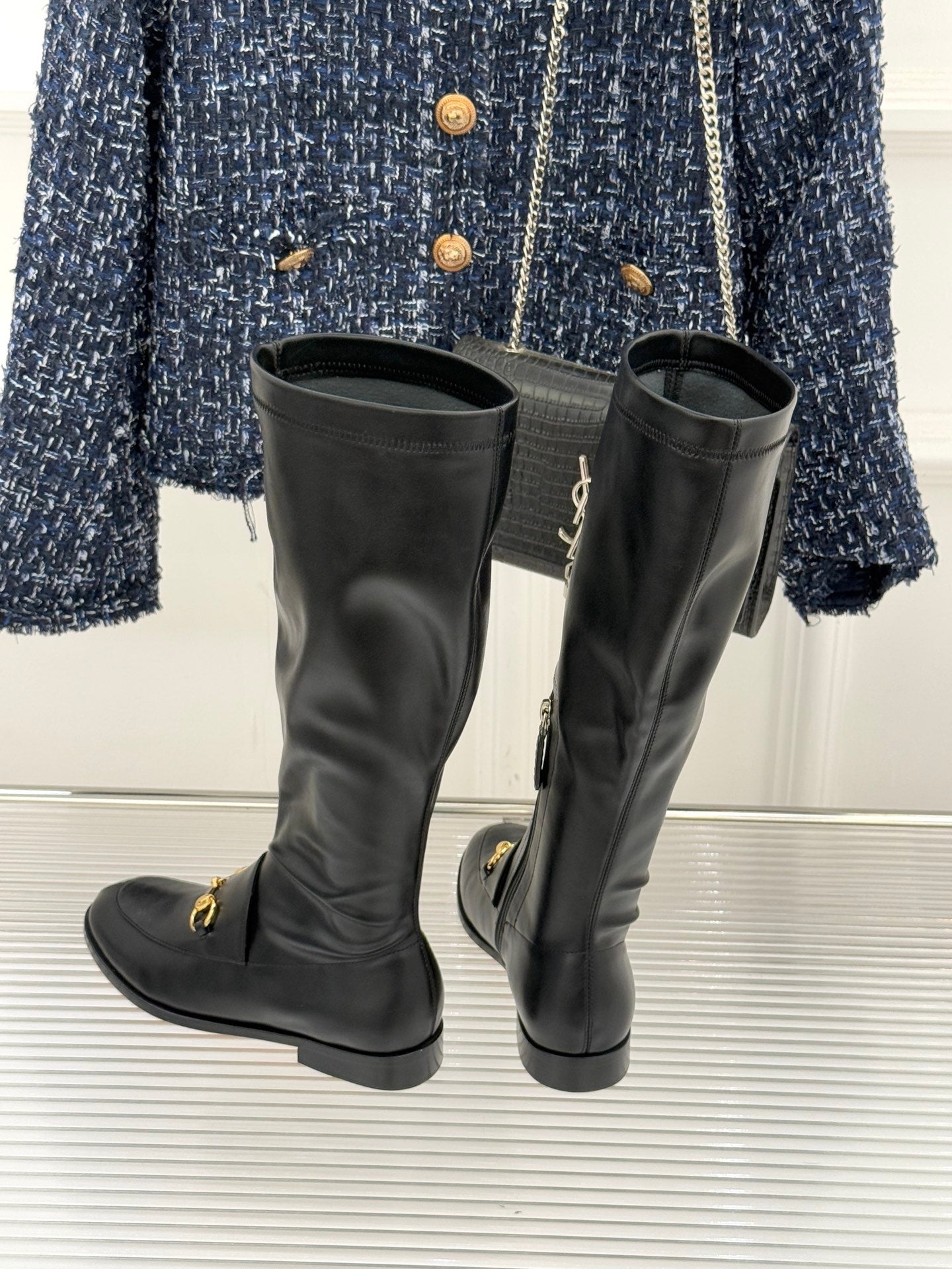 Black leather knee-high boots with gold horsebit detail and stacked heel