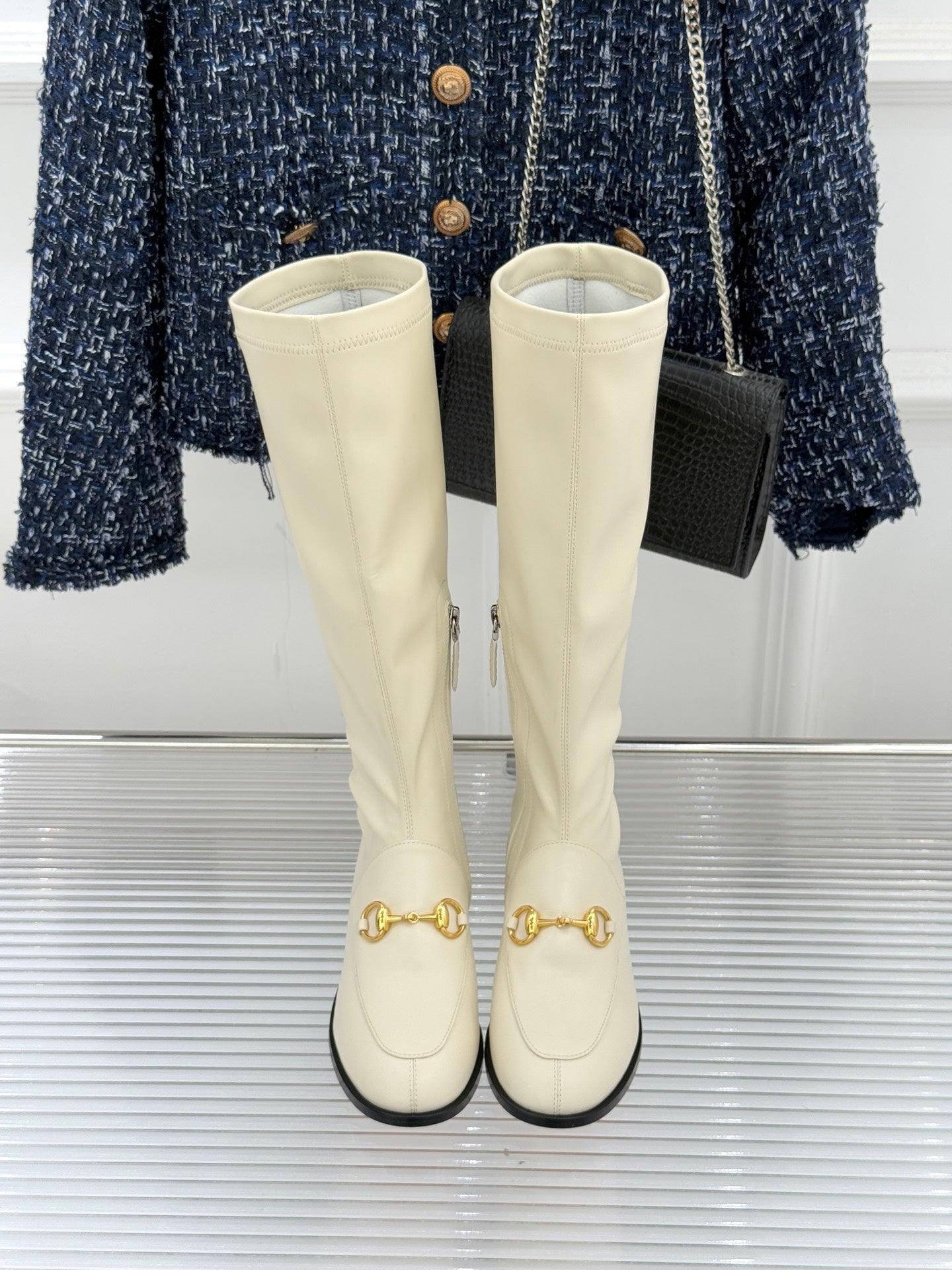 Women's off-white knee-high boots, front view, gold hardware on toes and black soles