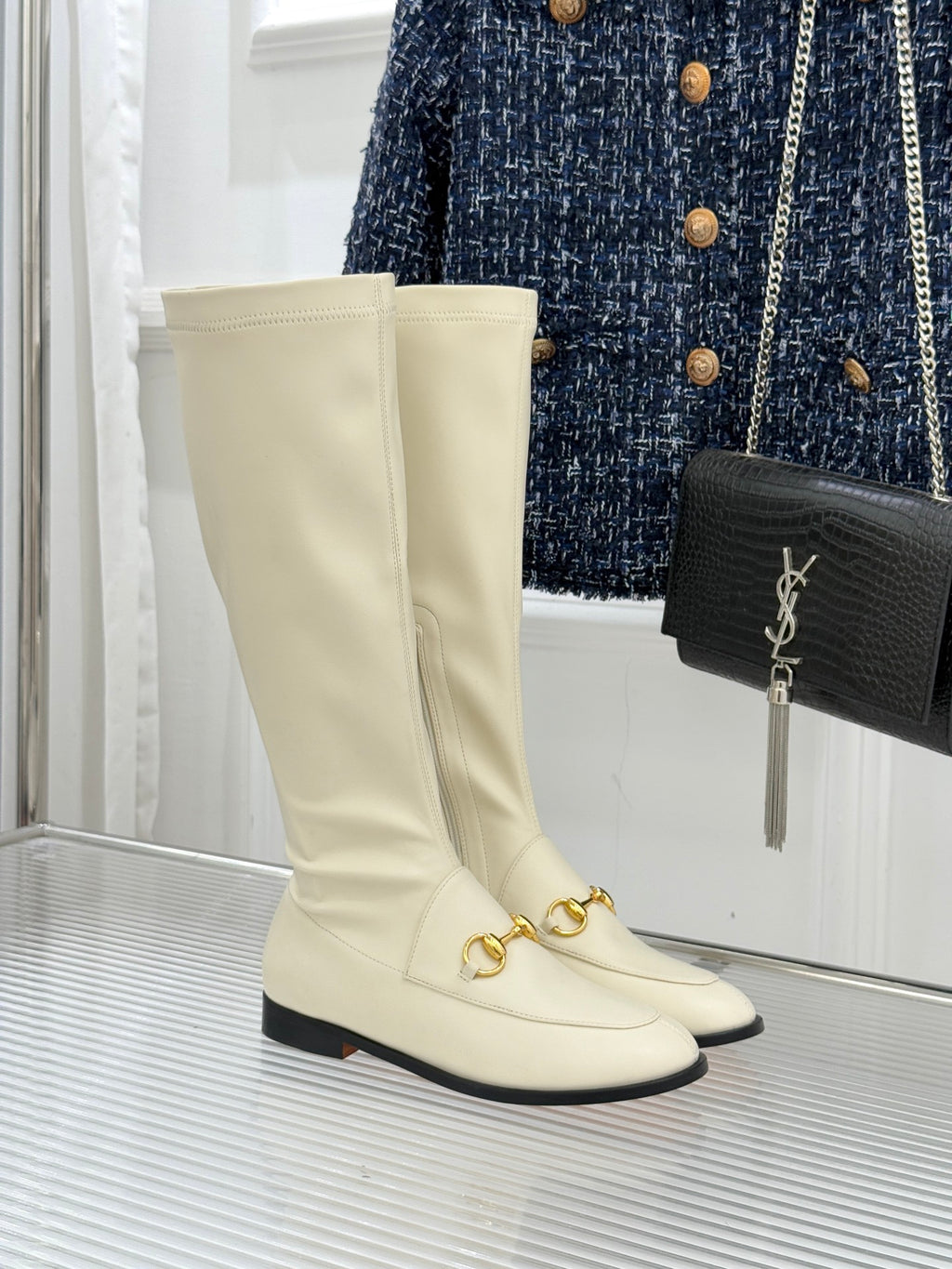 Women's off-white knee-high boots with gold buckle detail and black sole trim