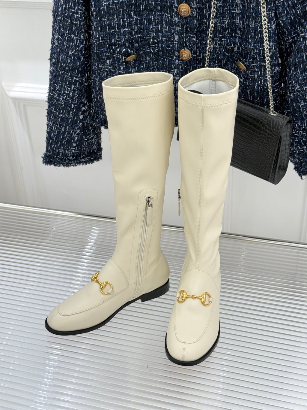 Women's off-white knee-high boots, side view, with gold strap hardware and black soles