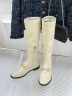 Women's off-white knee-high boots, side view, with gold strap hardware and black soles