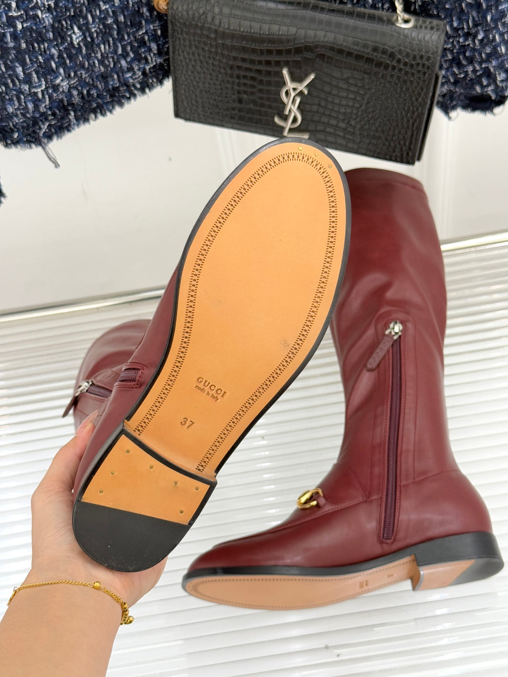 Maroon knee-high leather boots showing sole with Gucci logo and gold horsebit trim