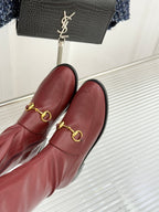 Maroon knee-high leather boots with gold horsebit strap detail near the top edge