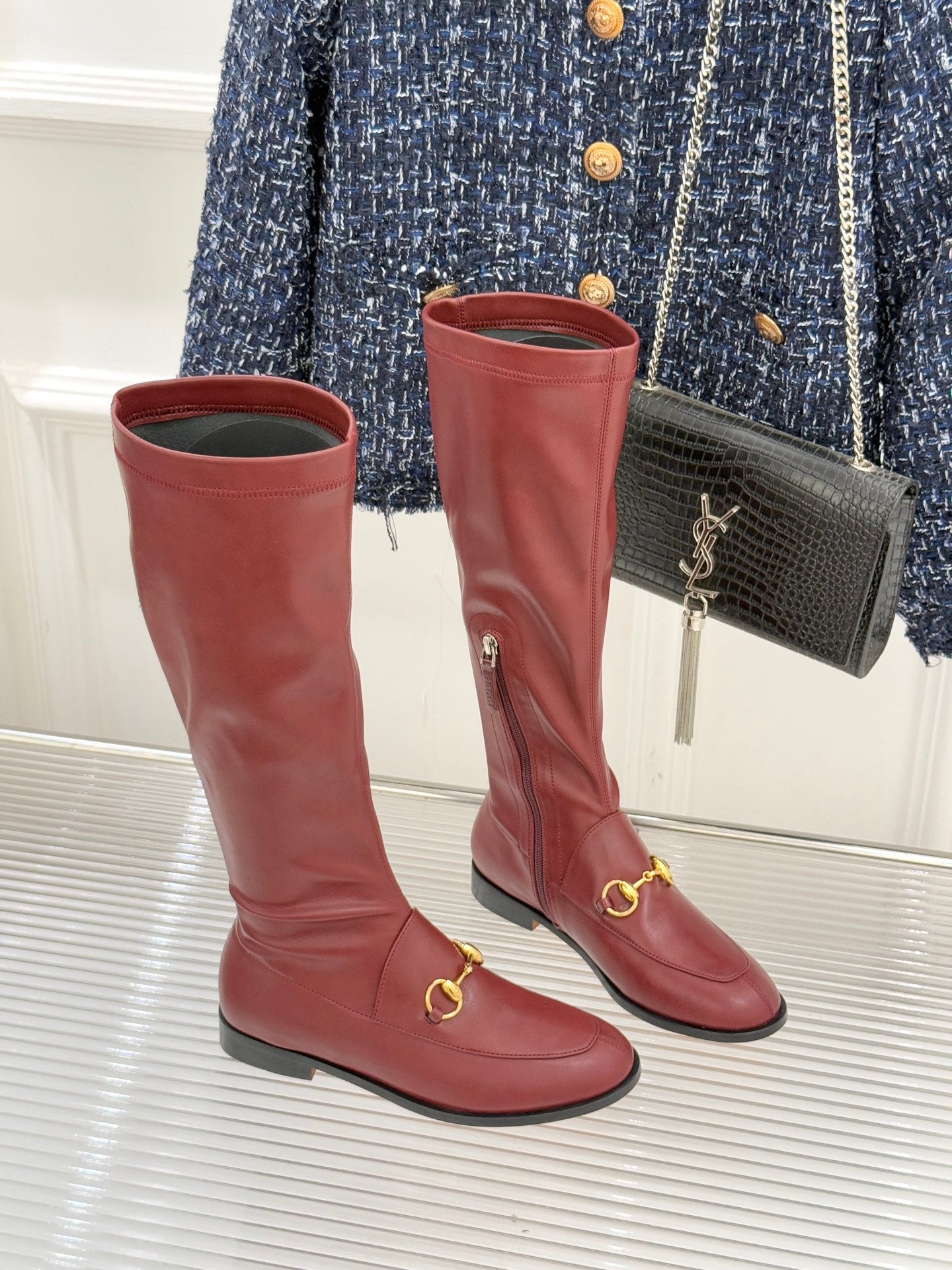 Maroon knee-high leather boots with gold horsebit strap detail and low block heel