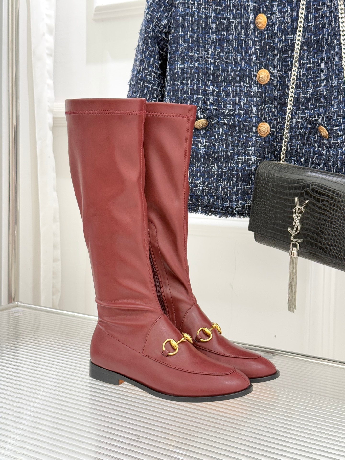 Maroon knee-high leather boots with gold horsebit hardware and low block heel