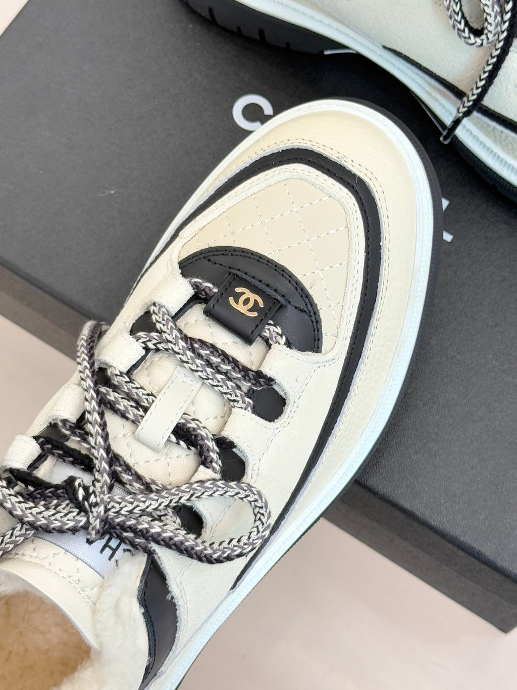 Side view of white Chanel sneaker with black heel tab and braided lace trim