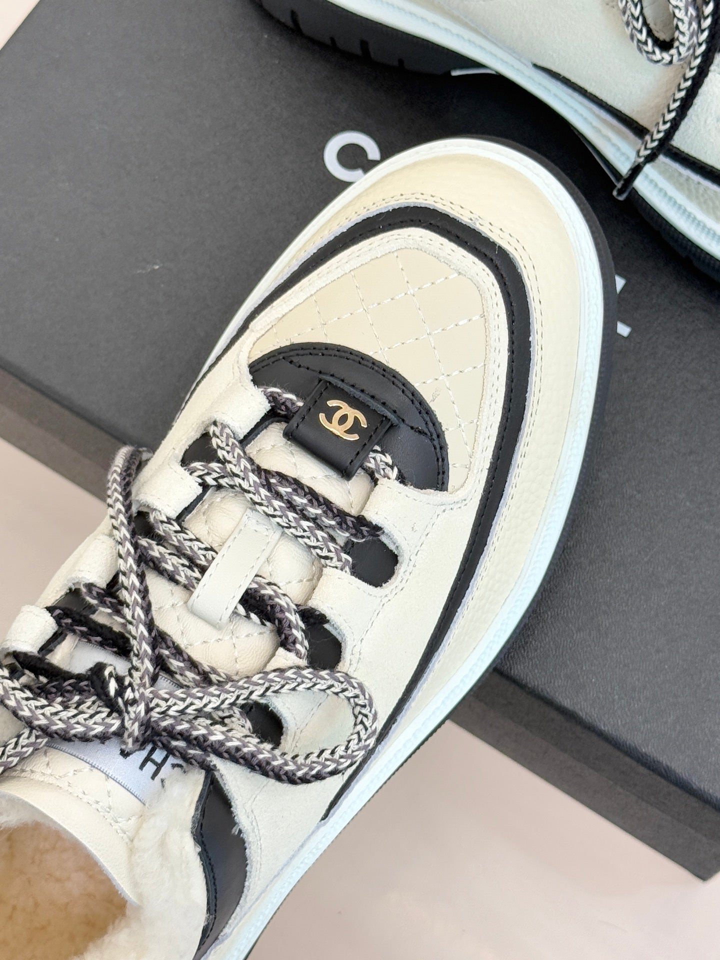 Side view of white Chanel sneaker with black heel tab and braided lace trim