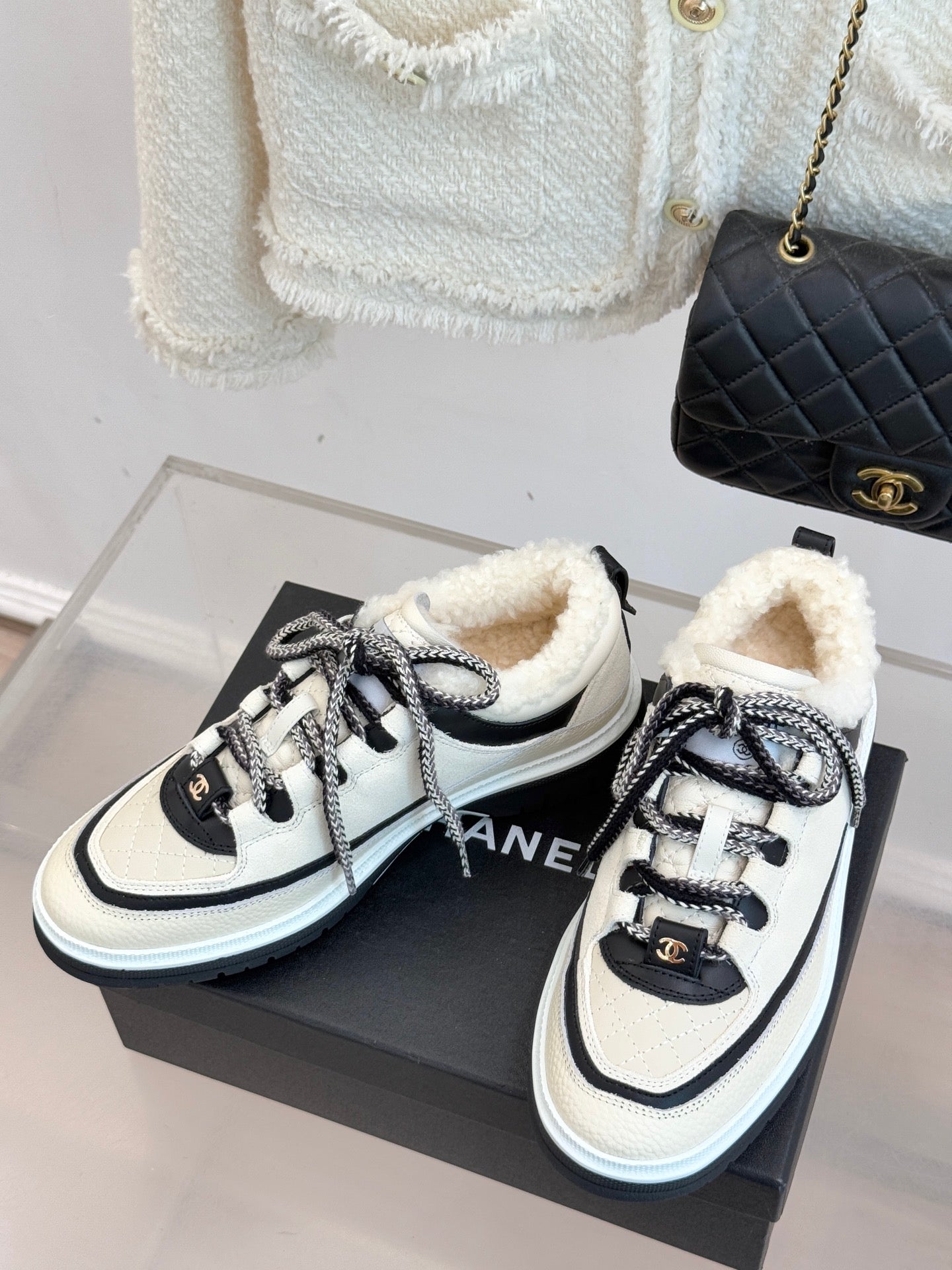 Pair of white Chanel sneakers with black details, lace-up closure, and fuzzy lining