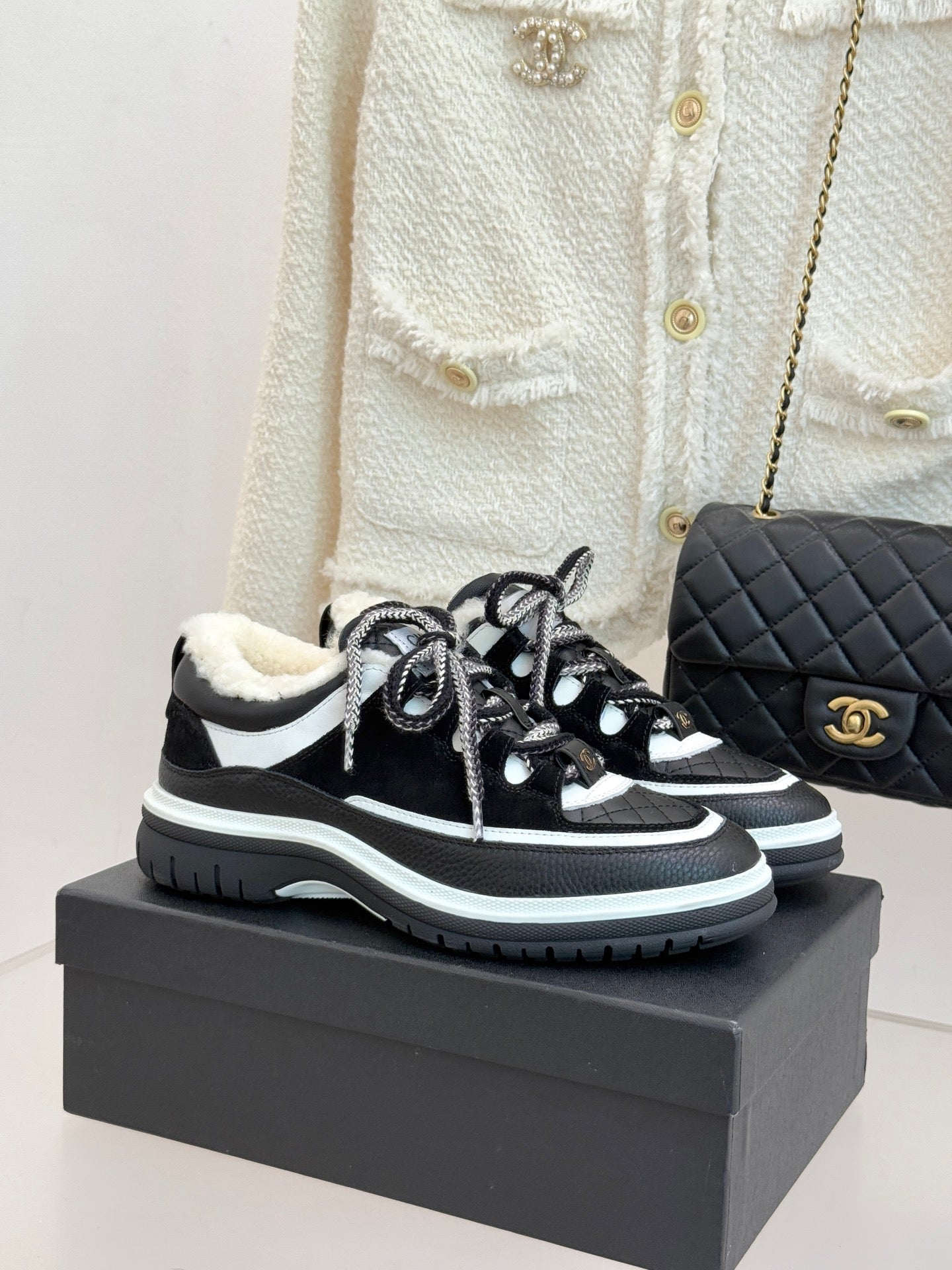 Black and white Chanel sneakers with shearling lining and chunky sole, laced up.
