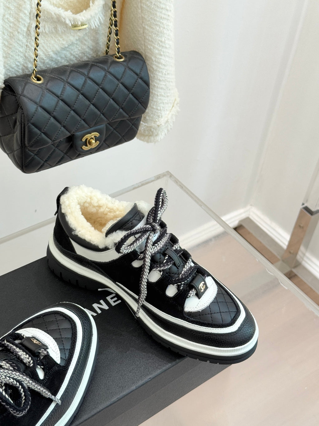 Black Chanel sneakers with white trim and shearling lining, angled view on box.