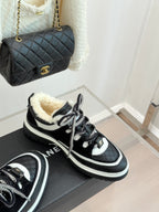 Black Chanel sneakers with white trim and shearling lining, angled view on box.