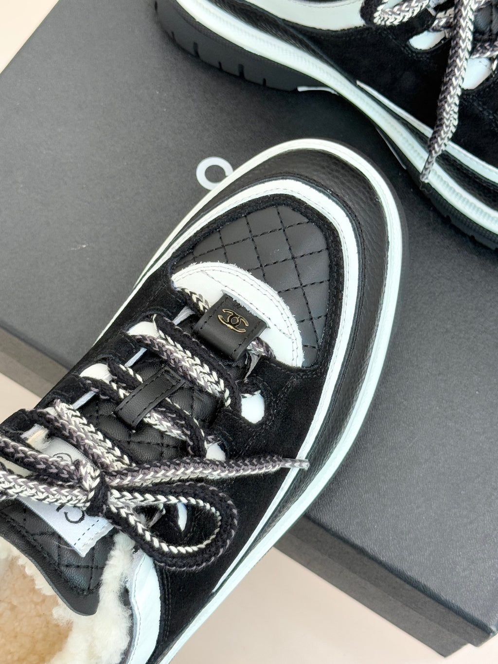 Black Chanel sneakers close-up showing logo tag, laces, and white-striped sidewall.