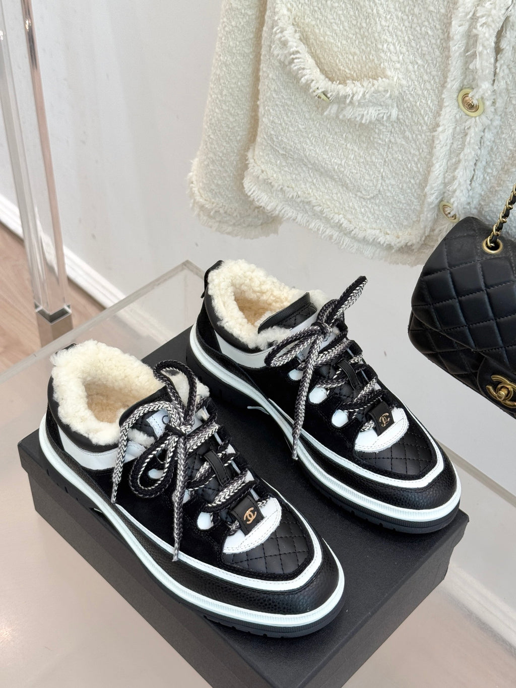 Pair of black Chanel sneakers with white piping and shearling-lined collars on box.