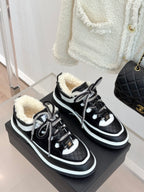 Pair of black Chanel sneakers with white piping and shearling-lined collars on box.