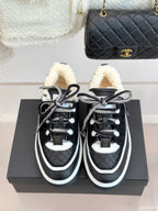 Black Chanel sneakers with white piping, shearling collars, and laces on display box.
