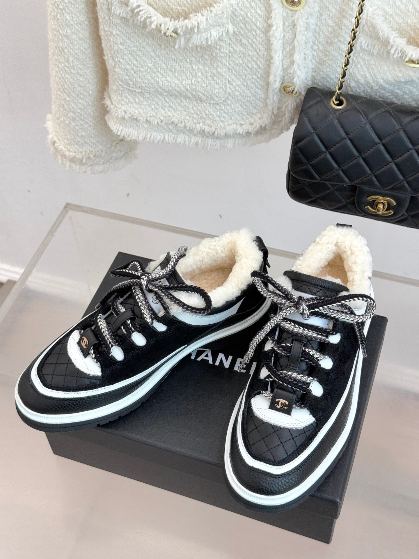 Black Chanel sneakers with white trim, shearling lining, and lace-up design on box.