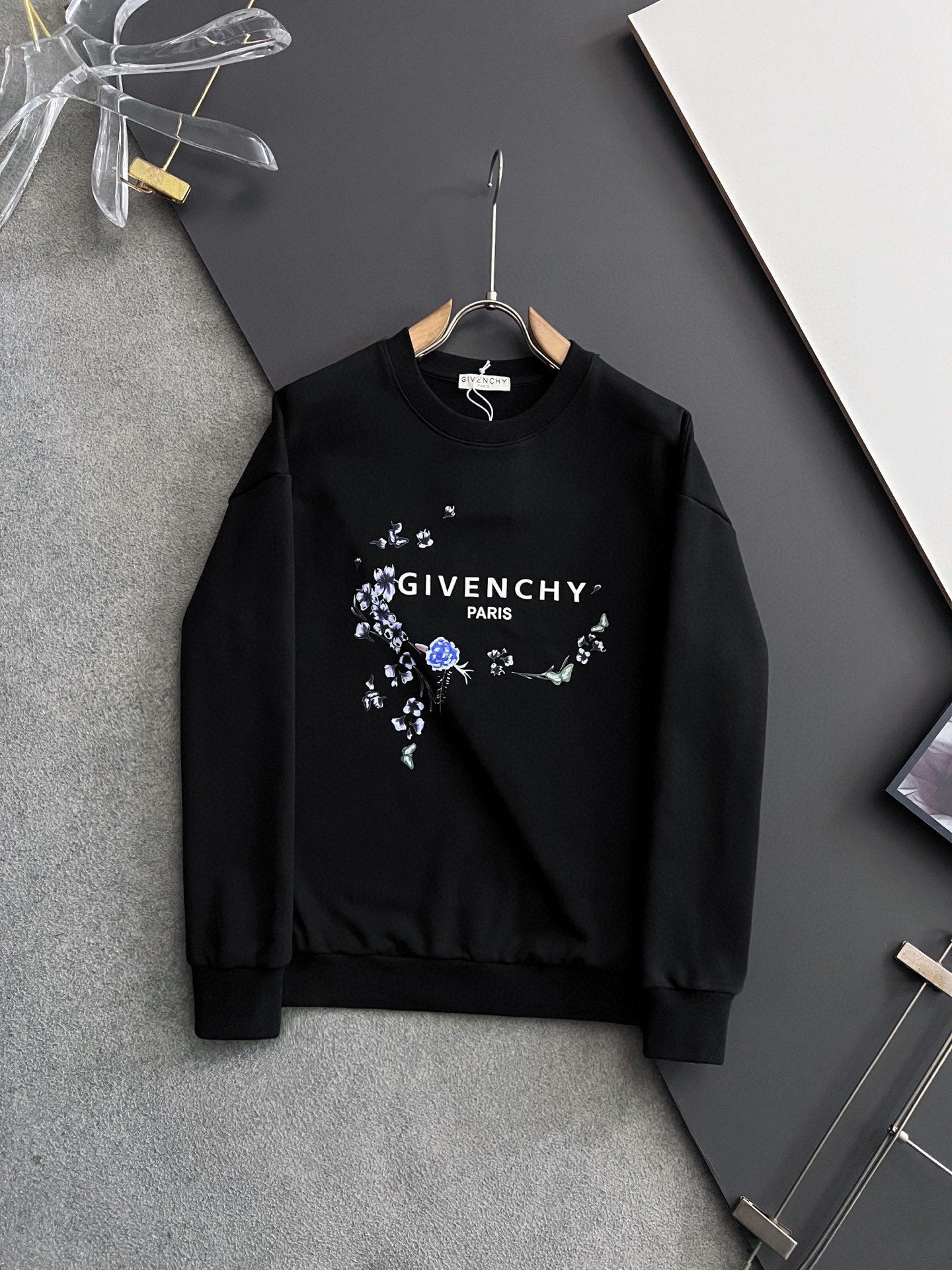 Black crewneck sweatshirt with blue floral wreath graphic and white chest text