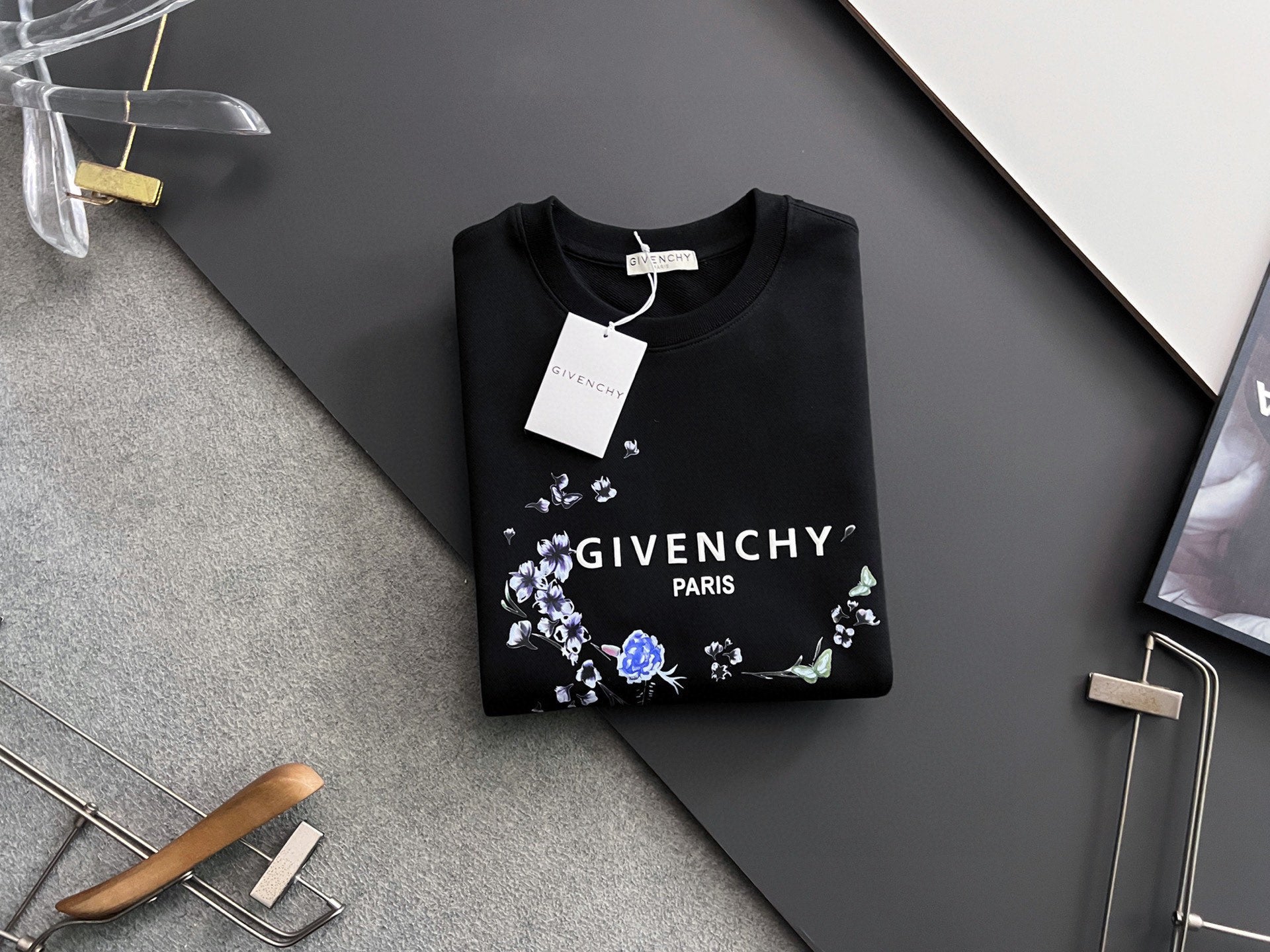 Black crewneck sweatshirt with floral wreath logo and hanging white tag
