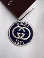 Circular Gucci logo patch on white sweatshirt fabric