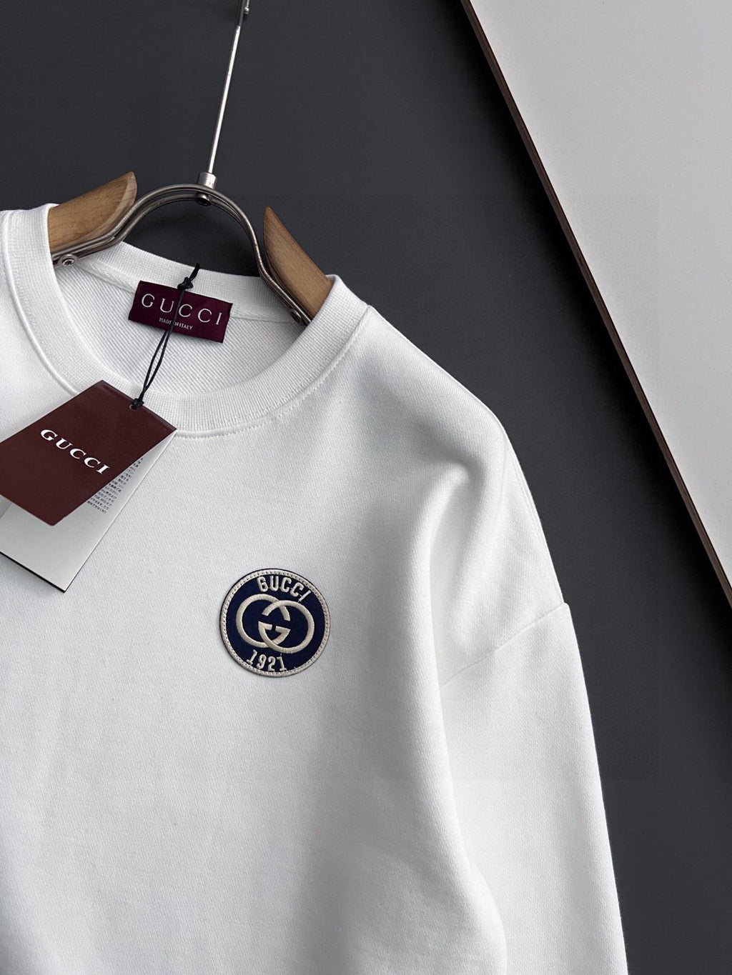 White crewneck sweatshirt with circular Gucci emblem patch on upper chest