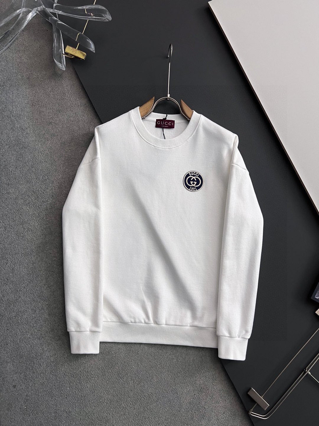 White crewneck sweatshirt with small circular Gucci logo patch on chest