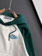 Two-tone hoodie close-up: green hood with white body and blue stitched graphic