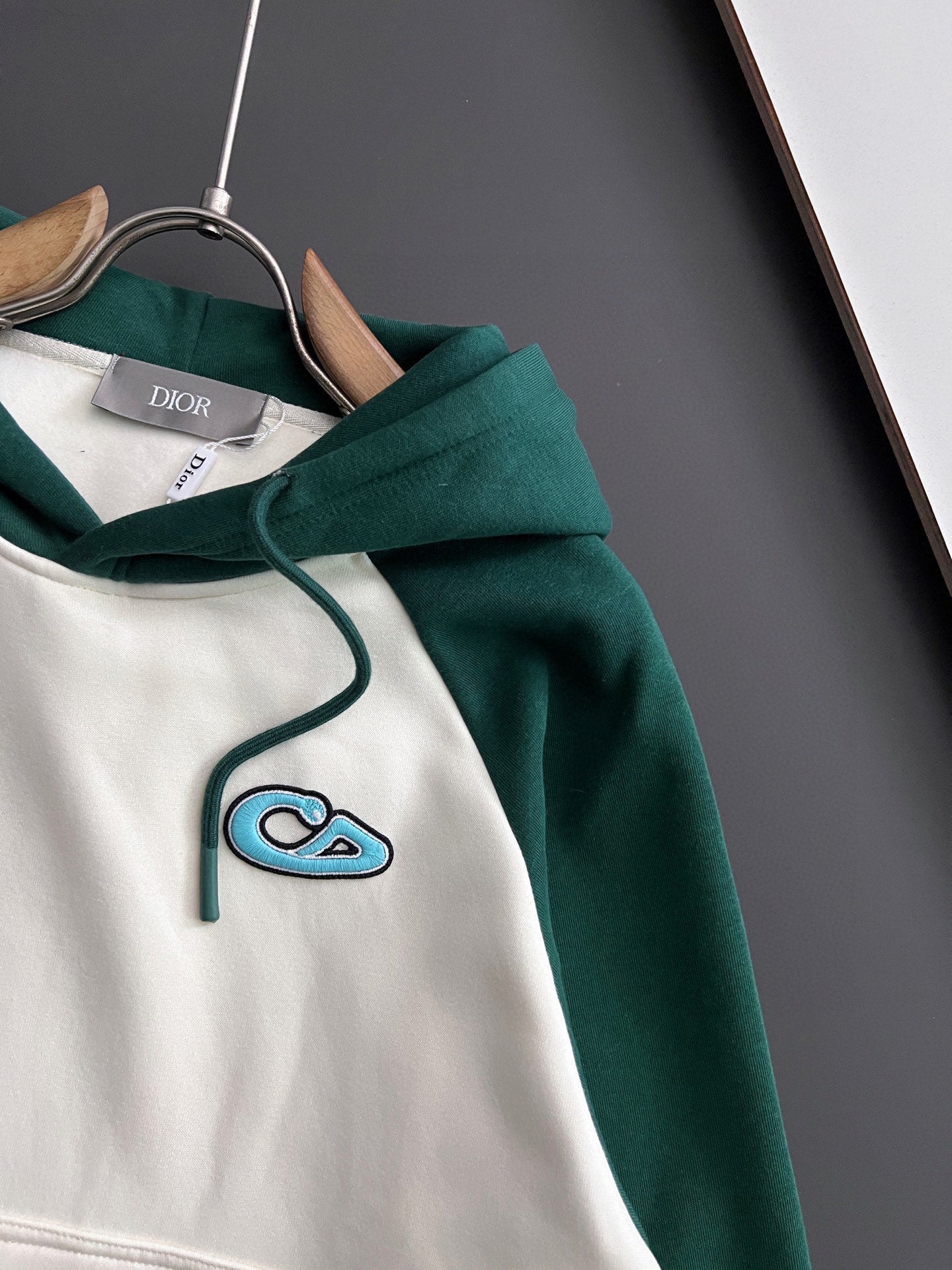 Two-tone hoodie close-up: green hood with white body and blue stitched graphic
