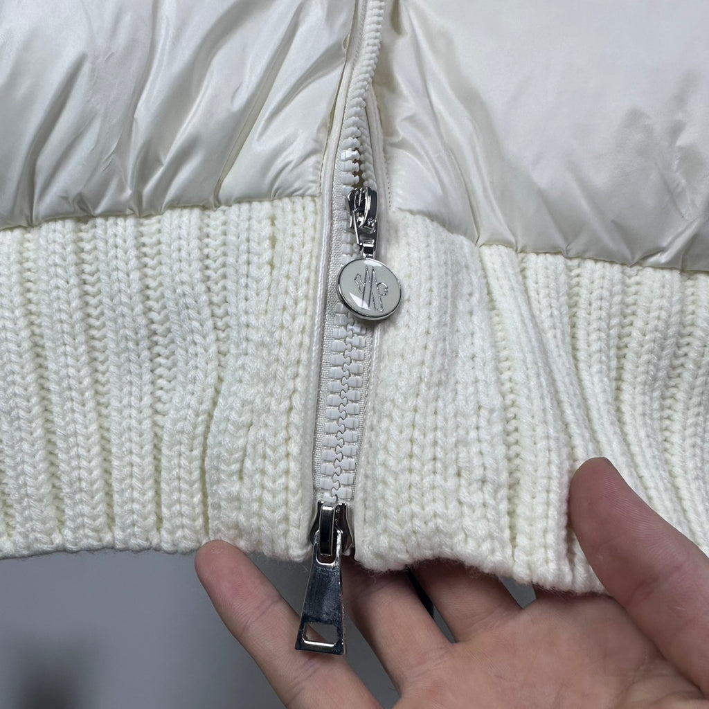 Long puffer jacket zipper close-up with silver pull and off-white knit hem