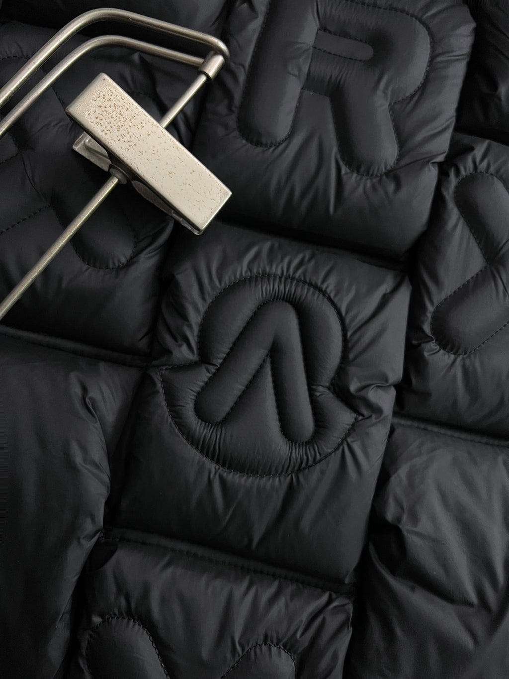 Close-up of black puffer jacket quilting with raised embroidered Moncler letters