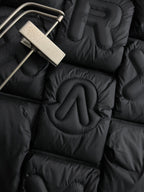 Close-up of black puffer jacket quilting with raised embroidered Moncler letters