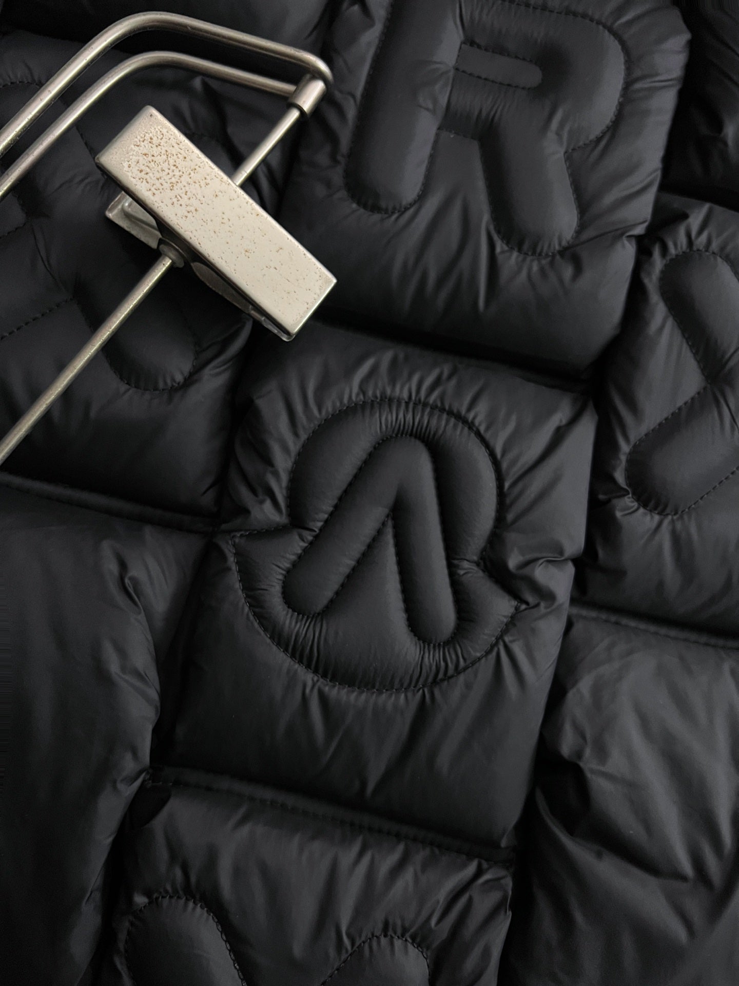Close-up of black puffer jacket quilting with raised embroidered Moncler letters