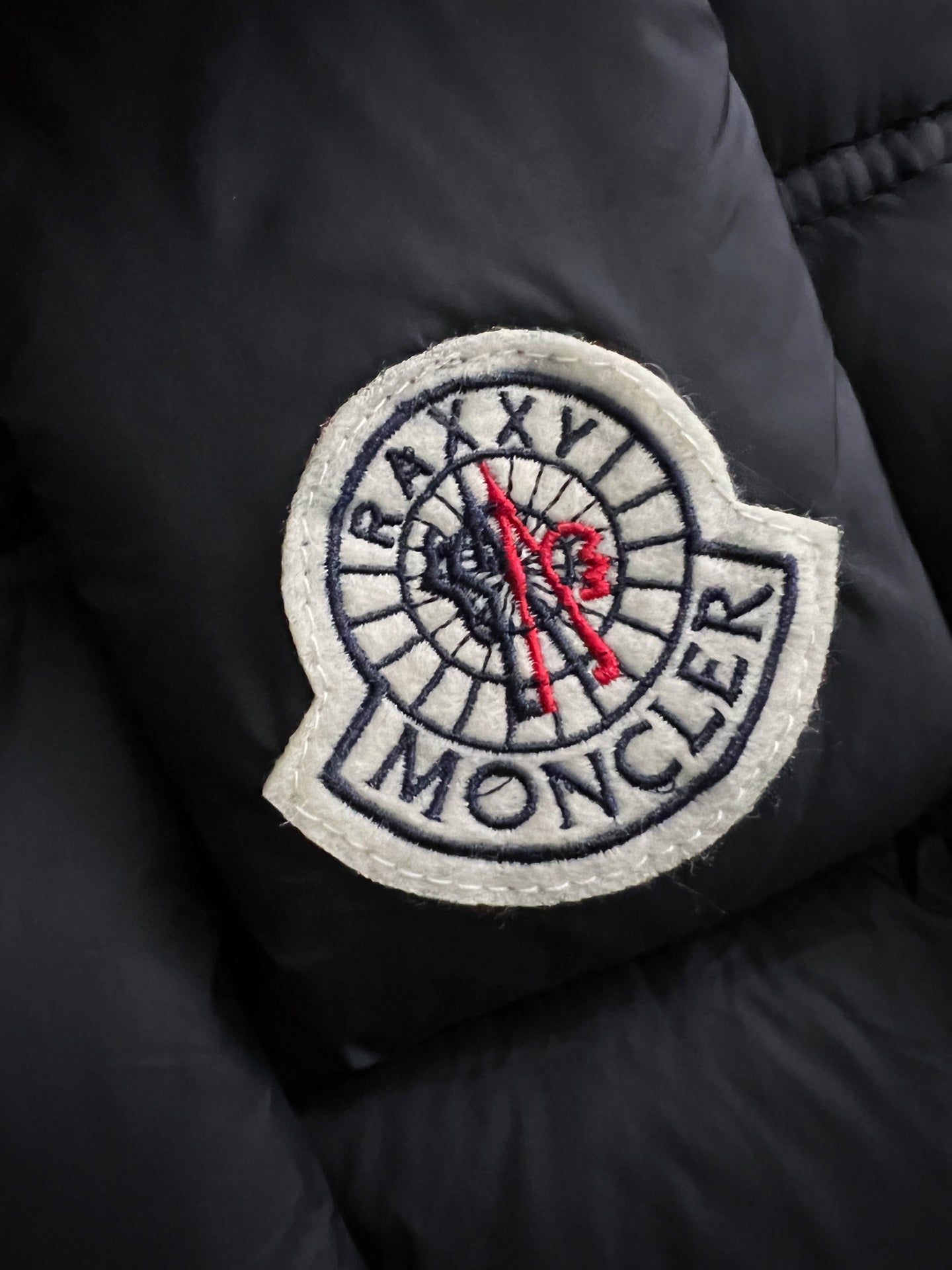 Moncler patch on black puffer fabric, red emblem with embroidered compass design