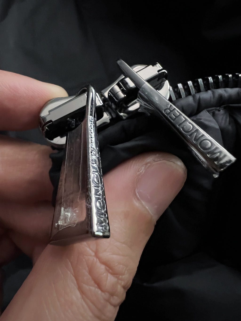 Metal snap and zipper pull on black puffer jacket, Moncler branding visible