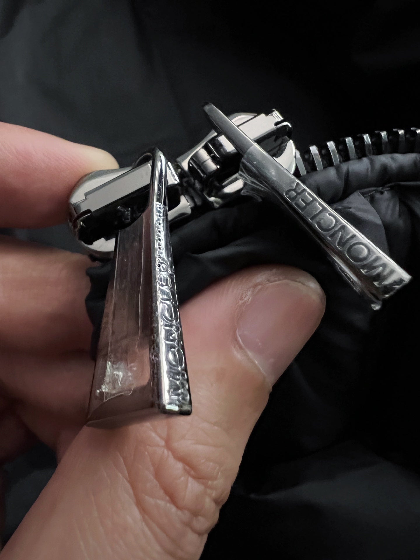 Metal snap and zipper pull on black puffer jacket, Moncler branding visible