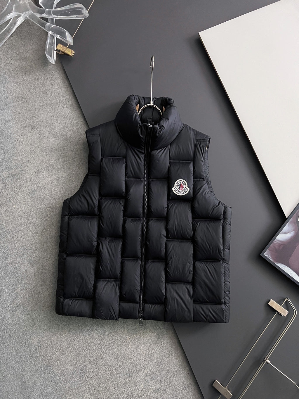 Black long puffer jacket with full zipper, hood, and side logo patch