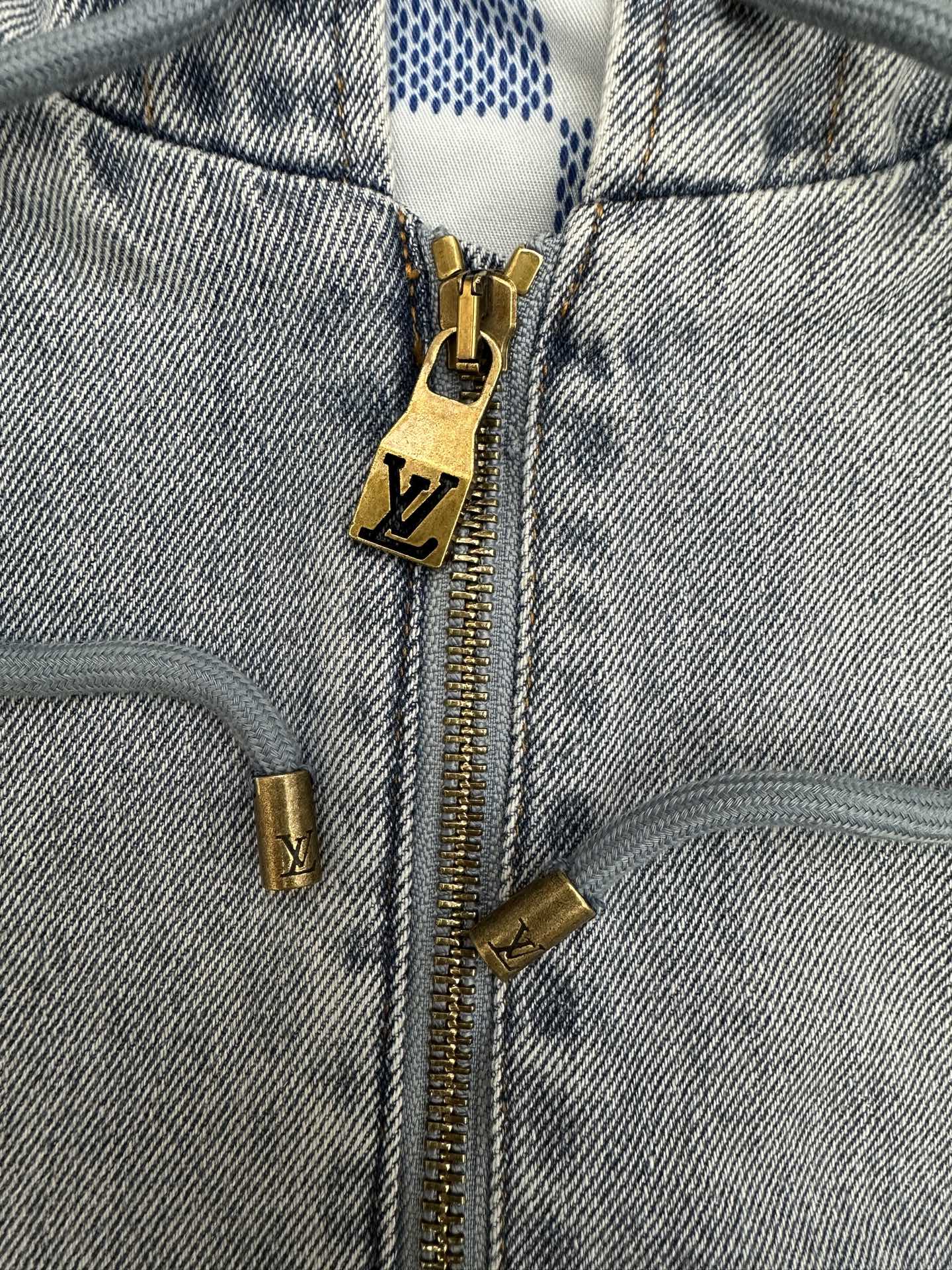 Denim zip-up jacket close-up with gold zipper and LV-logo charm